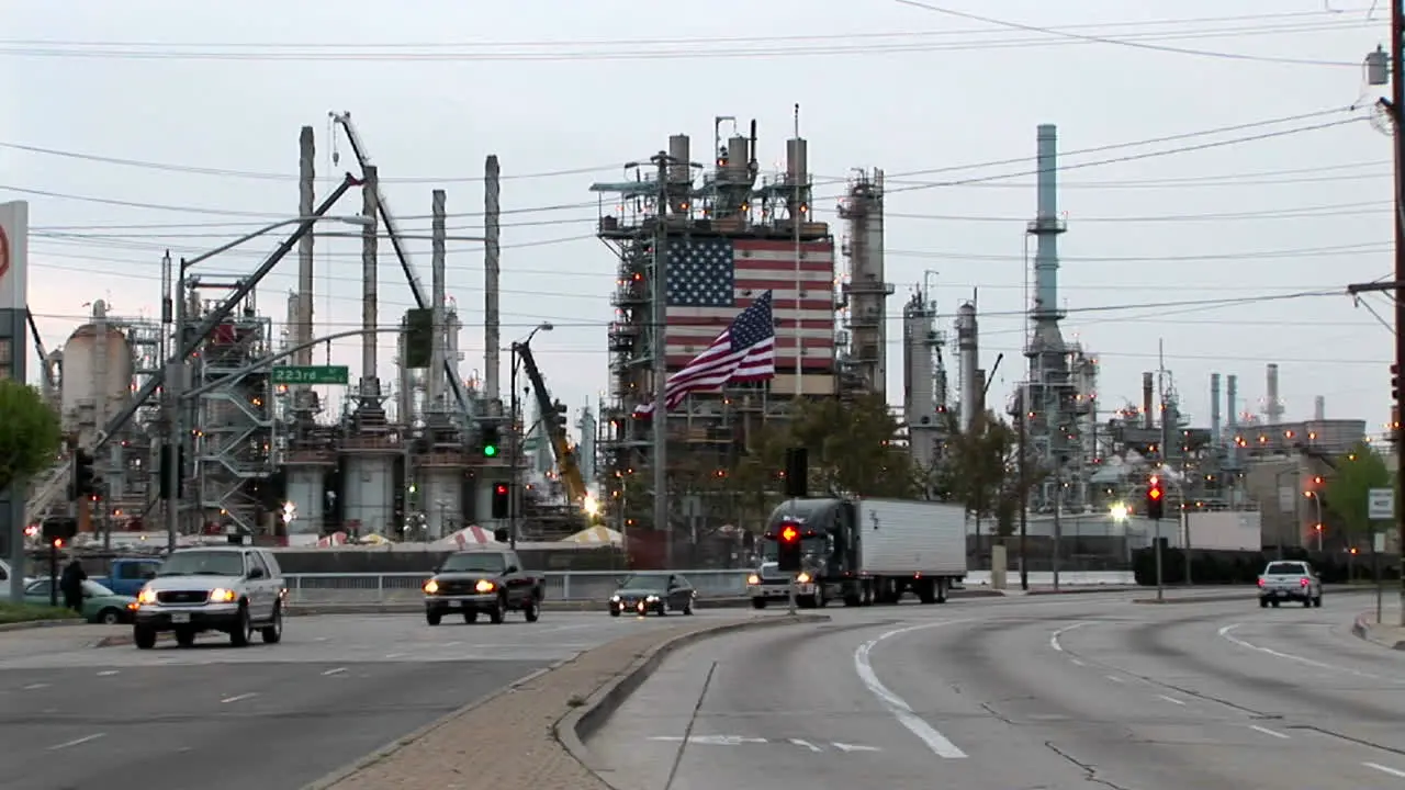 Traffic passes by an industrial plant adorned with two large American flags