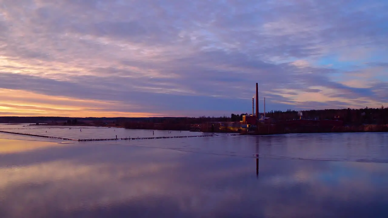 Cinematic aerial shot gliding towards a factory over glassy water reflections