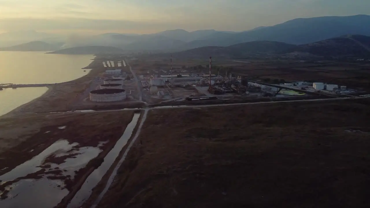 Aerial approach to oil refinery factory in a big valley by the sea at sunset