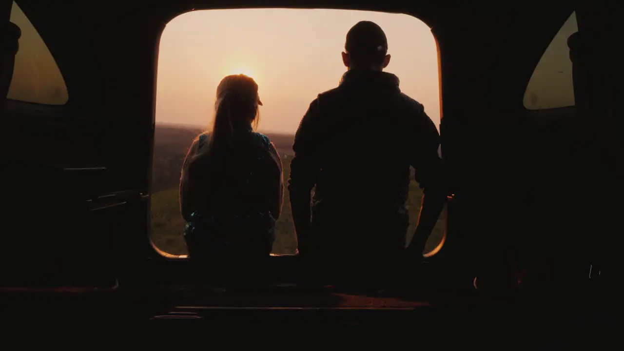 Teenager With Younger Sister Sitting In The Trunk Of A Car Watching The Sunset