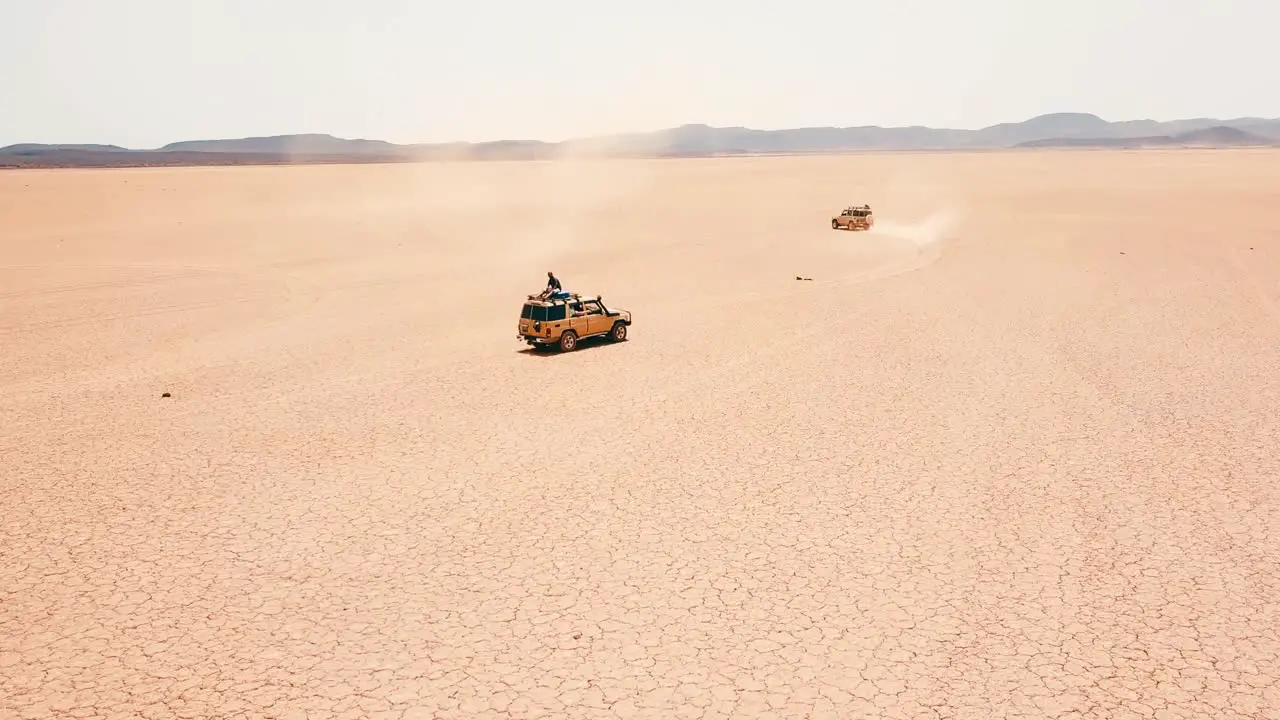 Good aerial of jeeps in road rally driving across Somalia with tourists leaning out and riding on roof celebrating