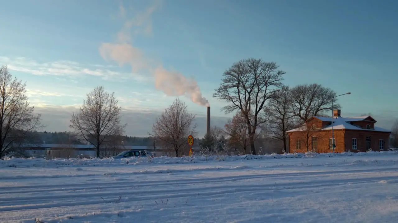 White smoke coming out of a tall chimney on a cold sunny winter while cars are driving by