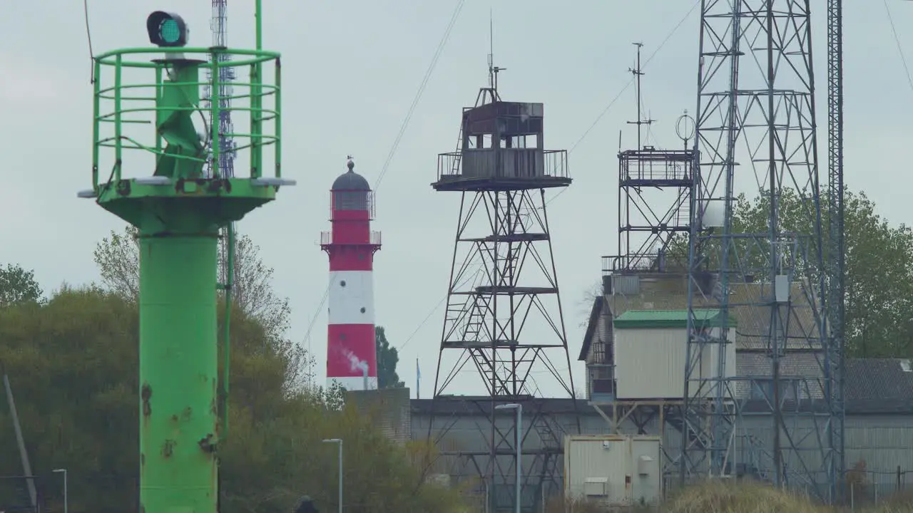 Red painted harbor lighthouse at Port of Liepaja on a overcast day distant view green port navigation beacon in foreground communication towers medium shot