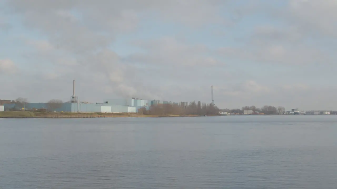 White smoke rising from industrial building on river shore wide