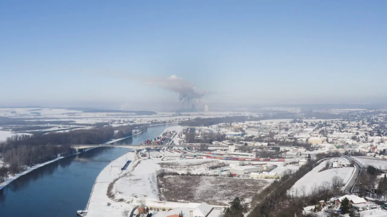 Smoking factory beyond a river town in winter snow cloudless Czechia