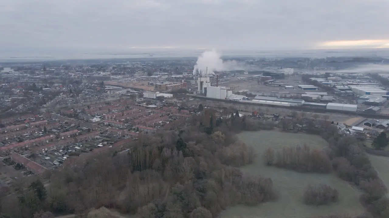 Flying over green park towards a polluting factory at the edge of city