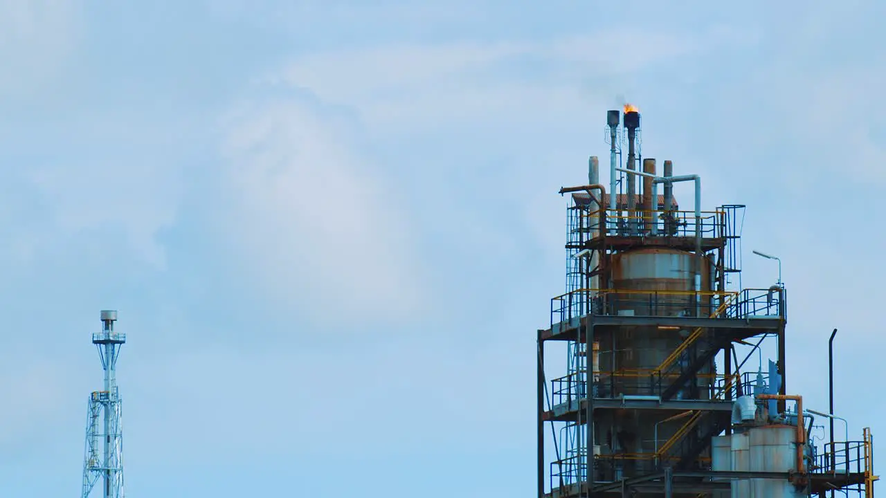 Slow motion shot of large industrial refinery with fire and black polluting smog pouring out the top into a clear blue sky in Curacao