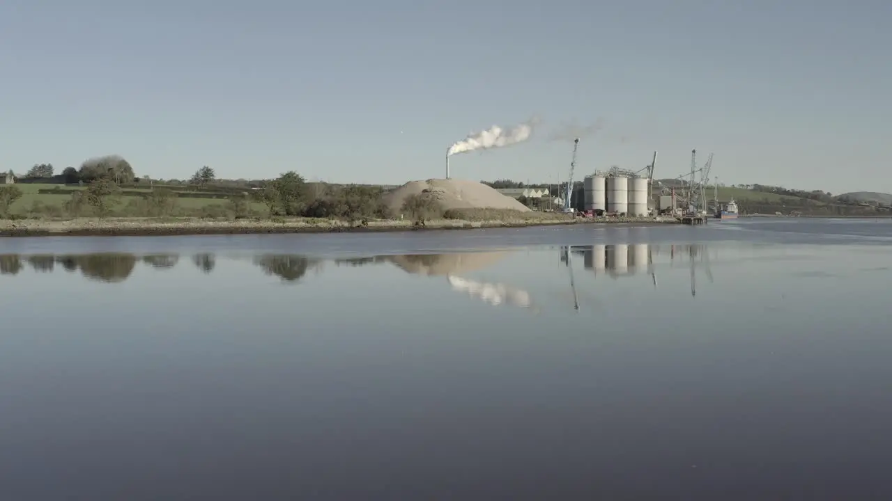 Riverside cement plant in Ireland with tall smoke stack seen beyond