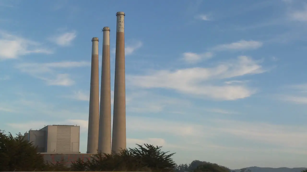 A time lapse shot of clouds moving behind the smokestacks of a power plant