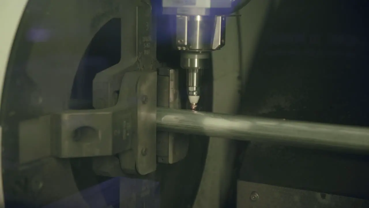 Slow motion footage of a laser cutting machine making holes and marks on a steel pipe