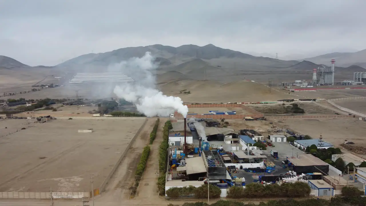 Drone orbits around a factory chimney with smoke plume rising up