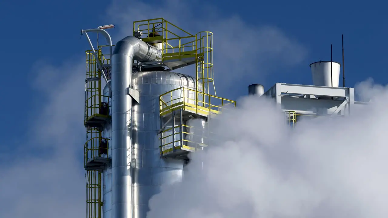 Steel tank tower in a chemical refinery covered by smoke against the blue sky