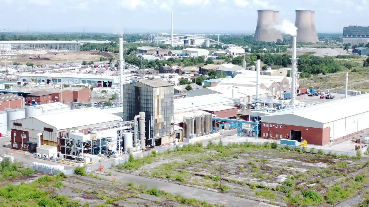 Industrial warehouse power plant refinery buildings under smokestack wasteland aerial view push in