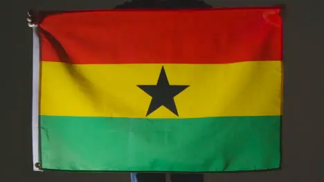 Studio Shot Of Anonymous Person Or Sports Fan Holding Flag Of Ghana Against Black Background