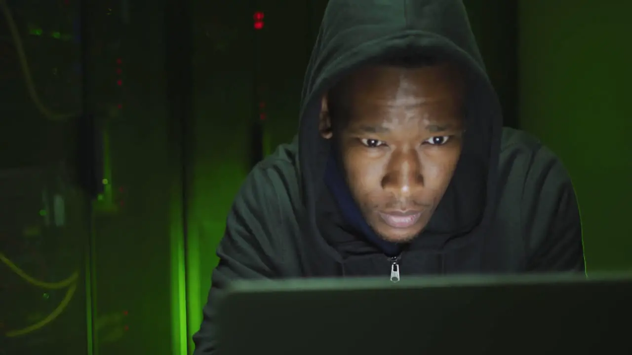 African american male computer hacker using laptop in business server room