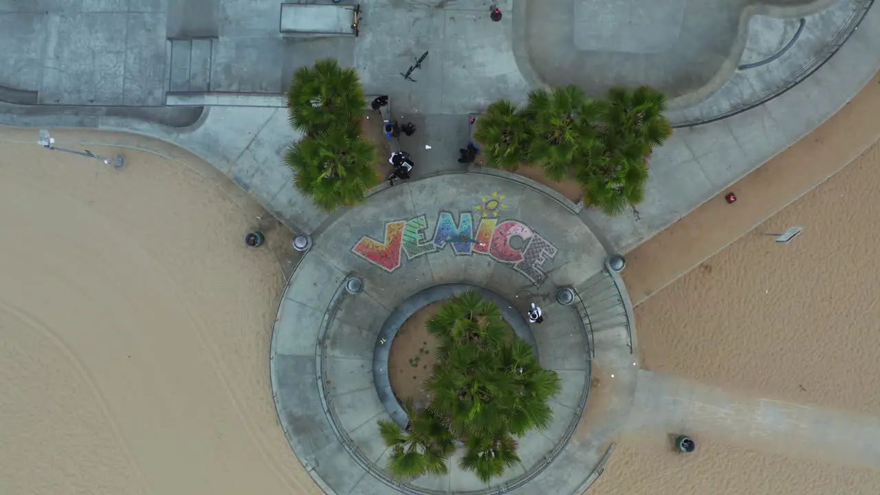 AERIAL Birds View of Man standing on Venice Sign in Skate Park Los Angeles California Cloudy