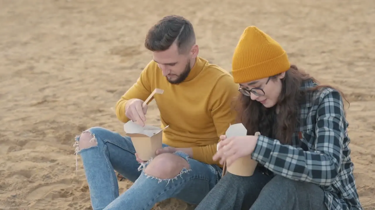 Young female and male friends eating take away food sitting on the beach