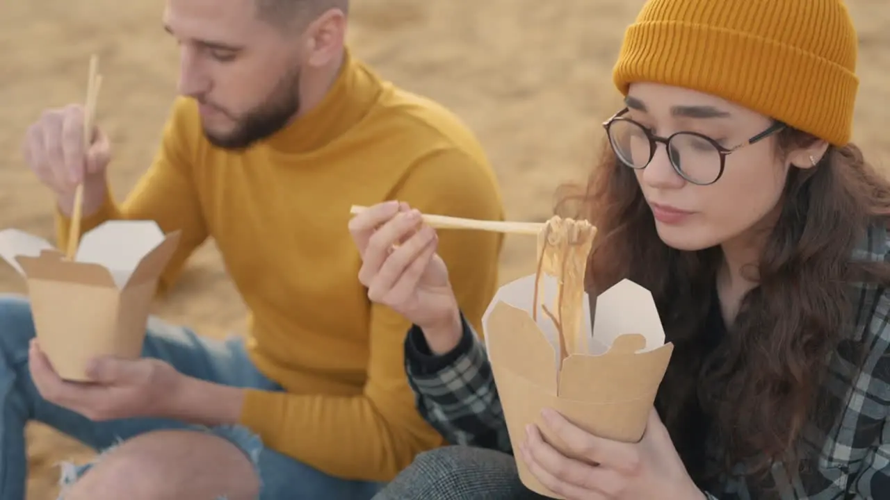 Young Female And Male Friends Eating Take Away Food Sitting On The Beach 1