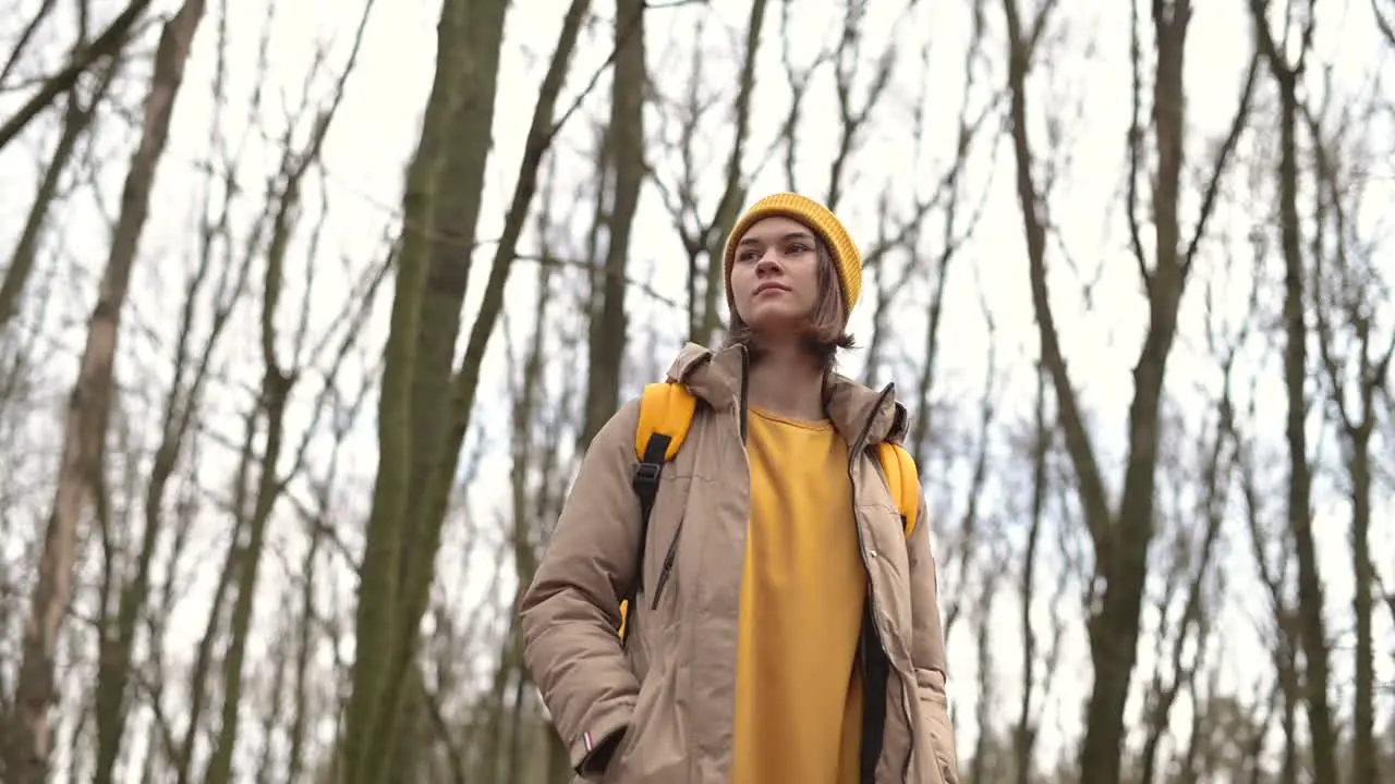 A Young Girl In A Yellow Wool Cap In The Forest Looks Up At The High Branches Of The Trees 1