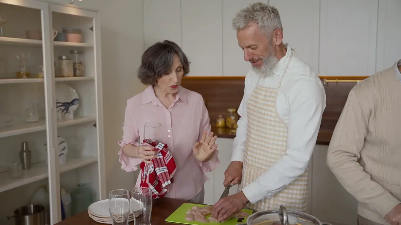 Older Man And Woman Friends Cooking And Talking In The Kitchen