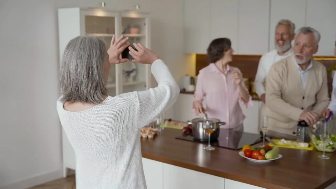 Happy Senior Woman On A Video Call While Her Friends Wave At The Camera While Laughing And Cooking