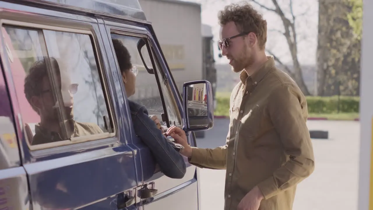 An Young Woman And A Young Man Have A Conversation While Refueling Their Van 2