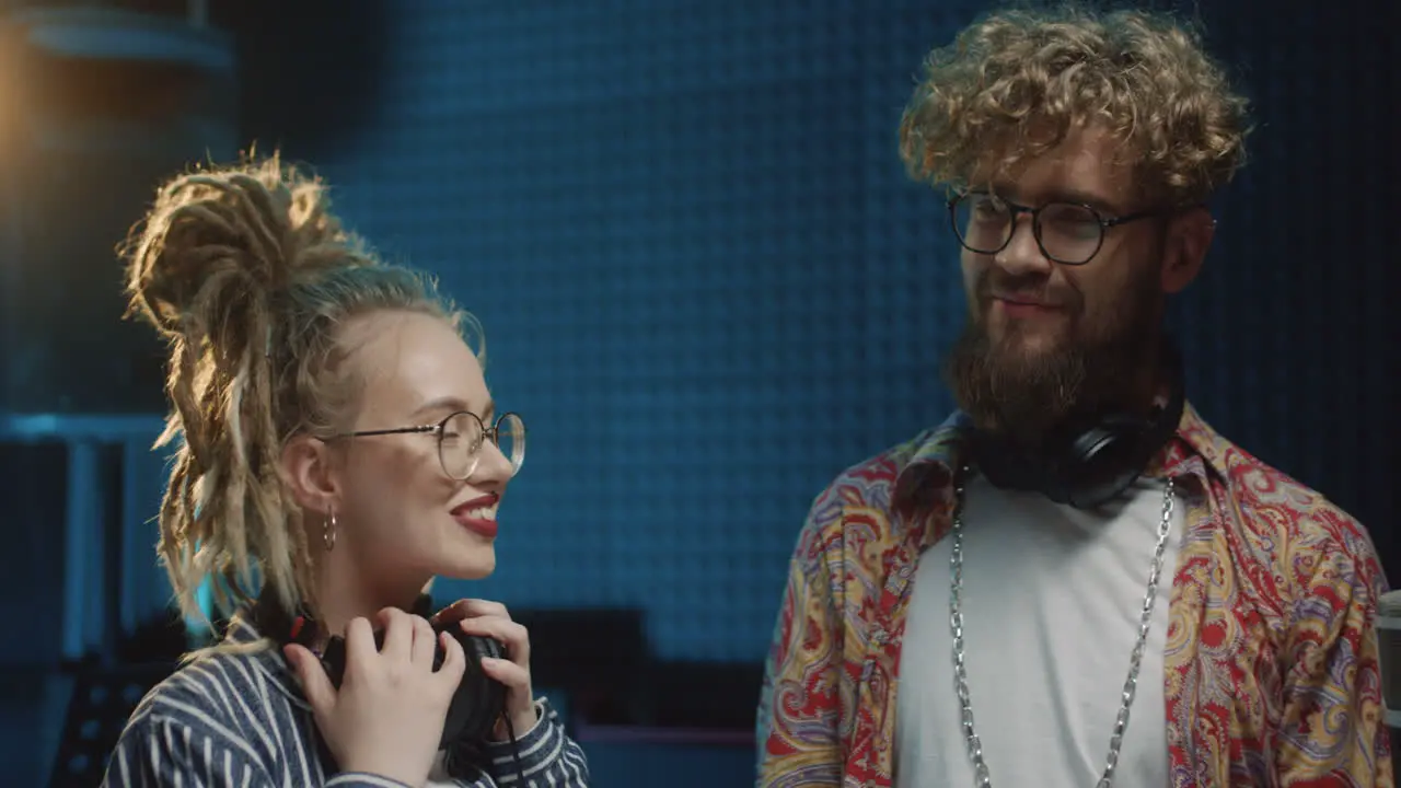 Portrait Shot Of The Happy Young Hipster Girl And Guy Standing At The Sound Studio With Headphones Getting Ready To Record And Smiling To The Camera