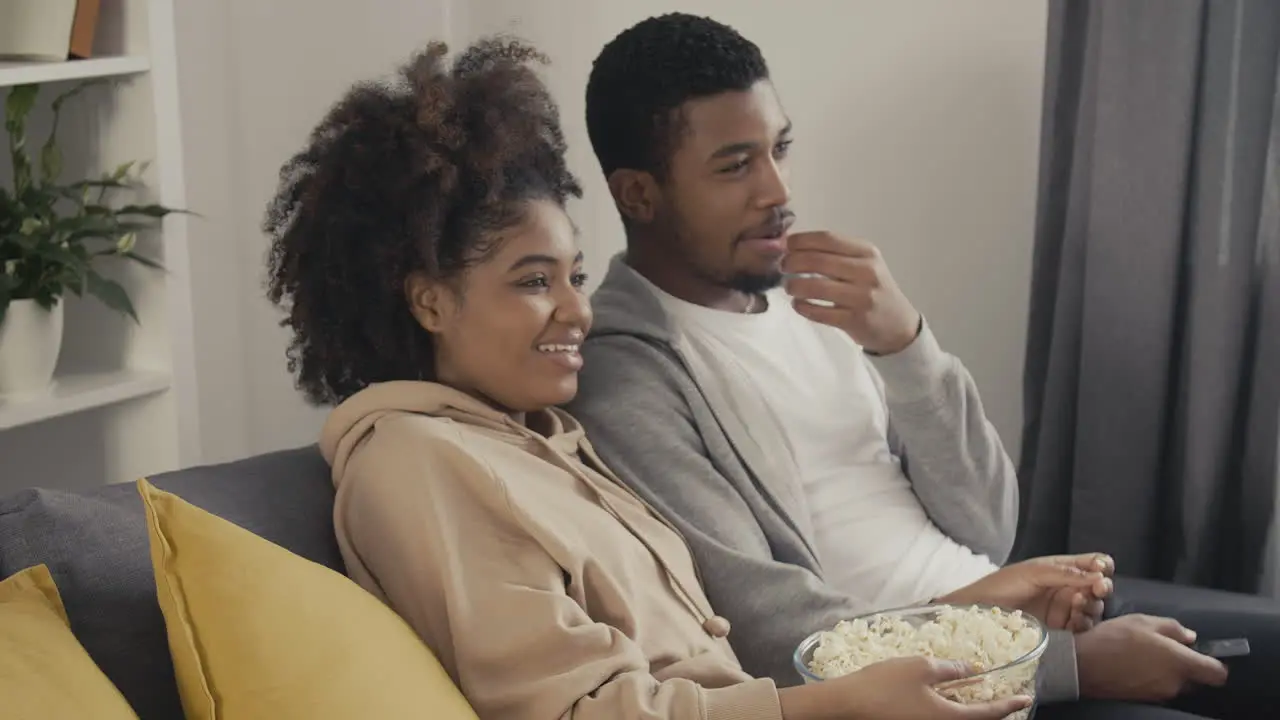 Young Couple Laughing While Watching A Film On Tv