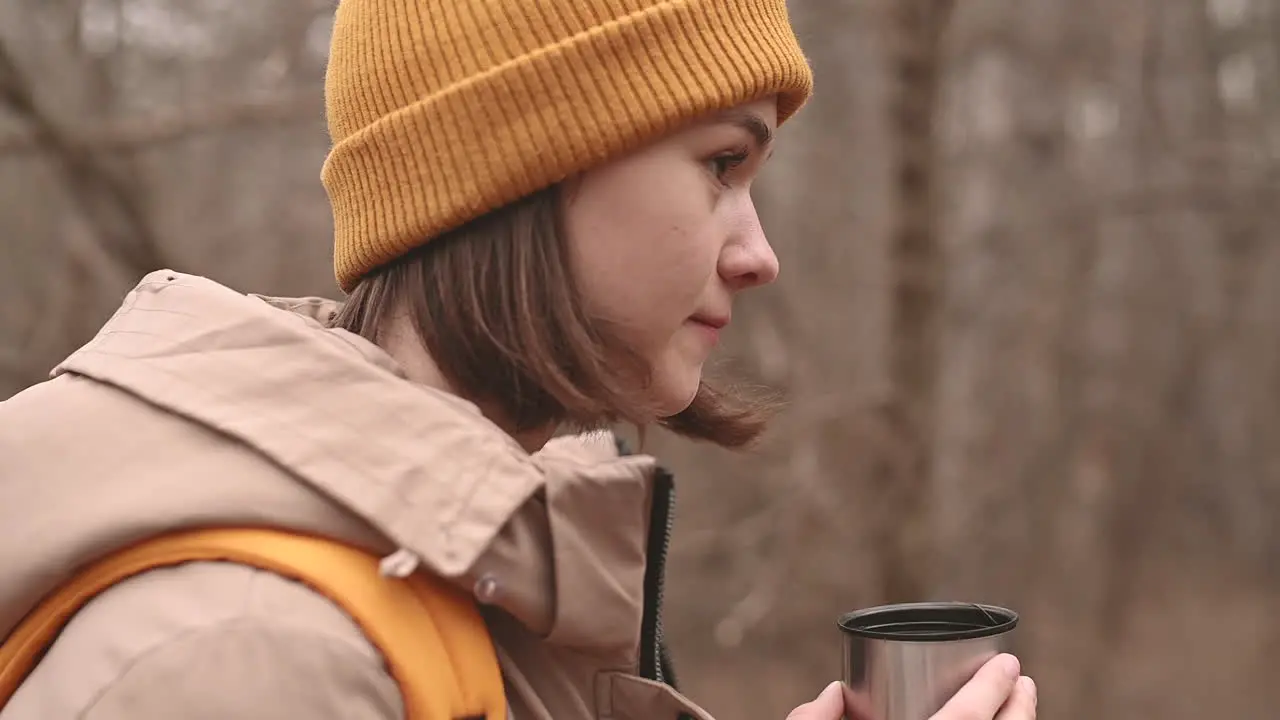 A Young Girl In A Yellow Woolen Hat Drinks A Hot Beverage In The Forest