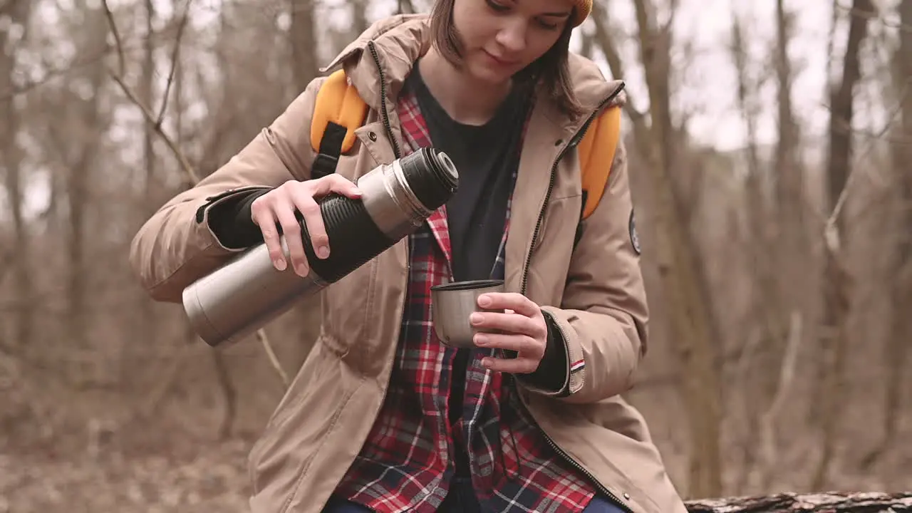 A Young Girl In A Yellow Woolen Hat Serves Herself A Hot Beverage In The Forest