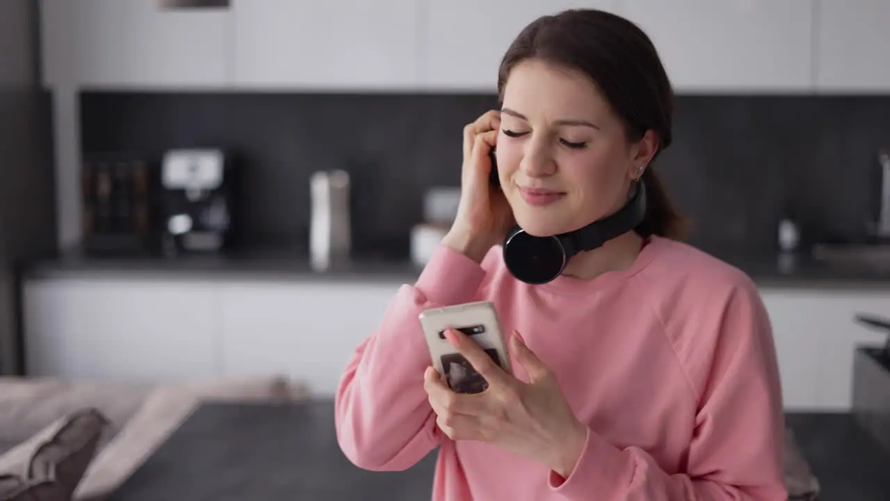 Pretty Young Woman In Headphones Dancing In Kitchen And Listening Music