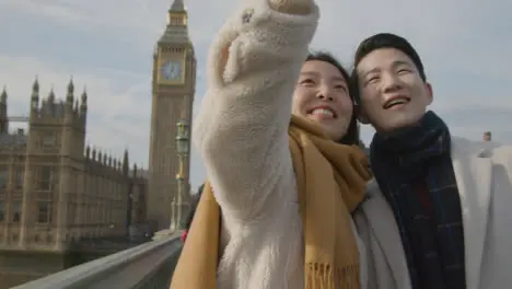 Young Asian Couple On Holiday Posing For Selfie In Front Of Houses Of Parliament In London UK 1