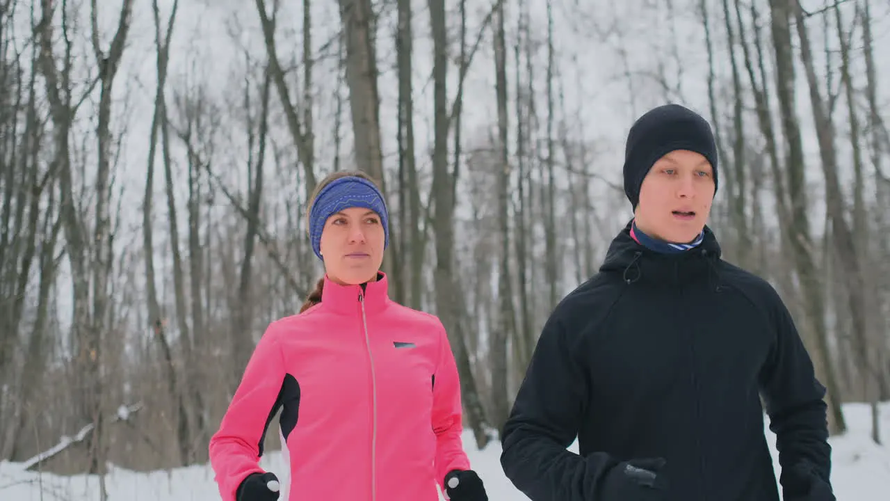 A man and a woman in a pink jacket in the winter running through the Park in slow motion Healthy lifestyle