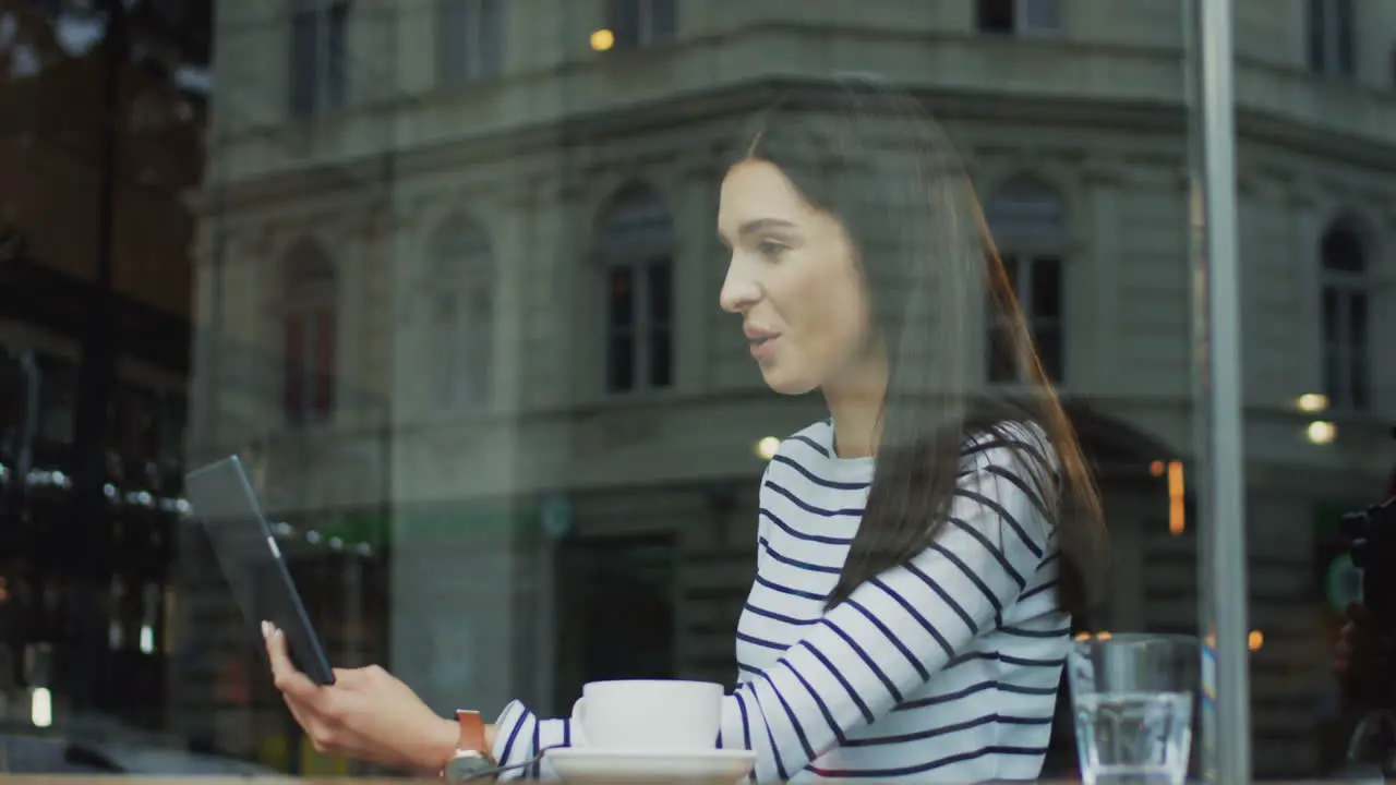 Brunette Young Woman Sitting In The Cafe And Having Videochat On The Tablet Talking And Being Cheerful