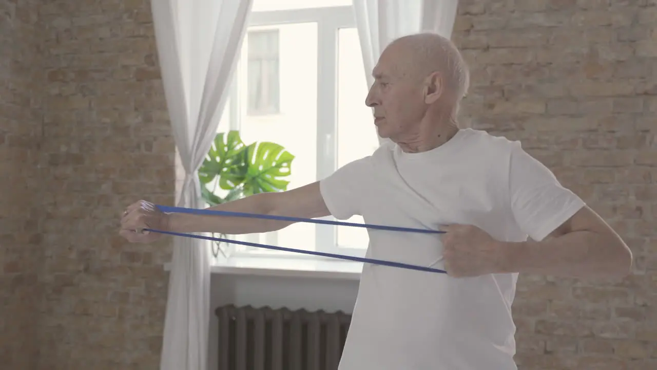 Old Man Using A Stretching Band And Exercising At Home