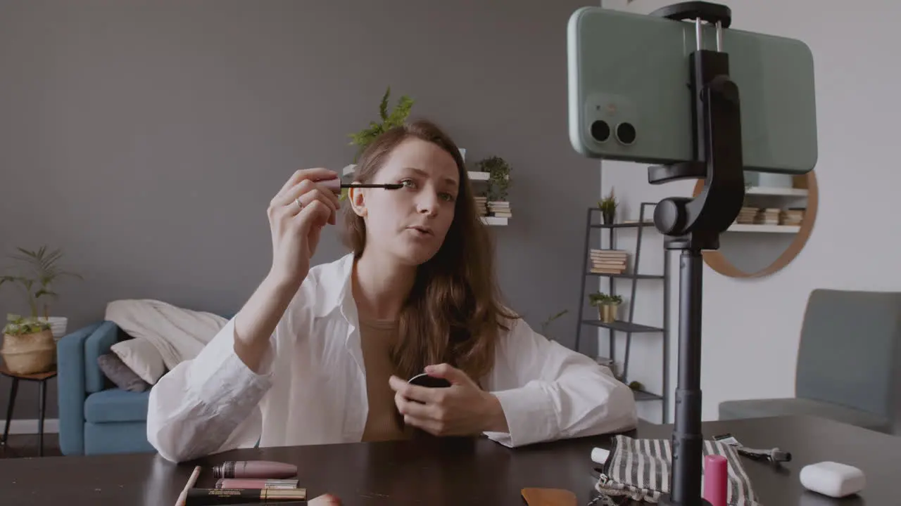 Young Beautiful Vlogger Female Recording An Eye Mascara Review In Front Of Her Smartphone Camera