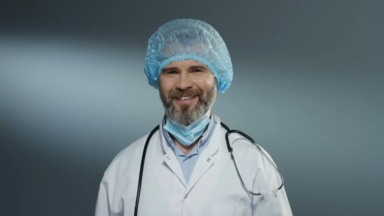 Portrait Shot Of The Handsome Man Doctor In Blue Hat Taking Off Mask From His Mouth And Smiling Cheerfully To The Camera