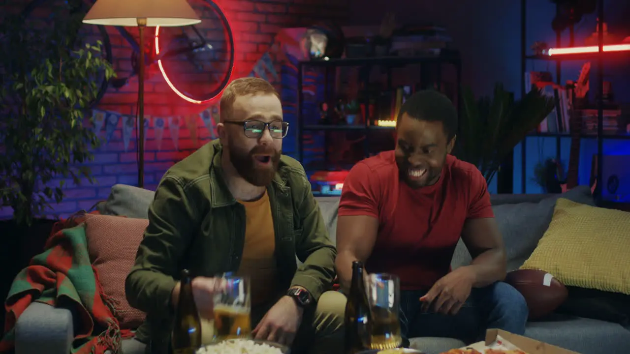 Two Mixed Races Cheerful Men Watching Sport Match On Tv Drinking Beer And Being Happy As Their Team Won