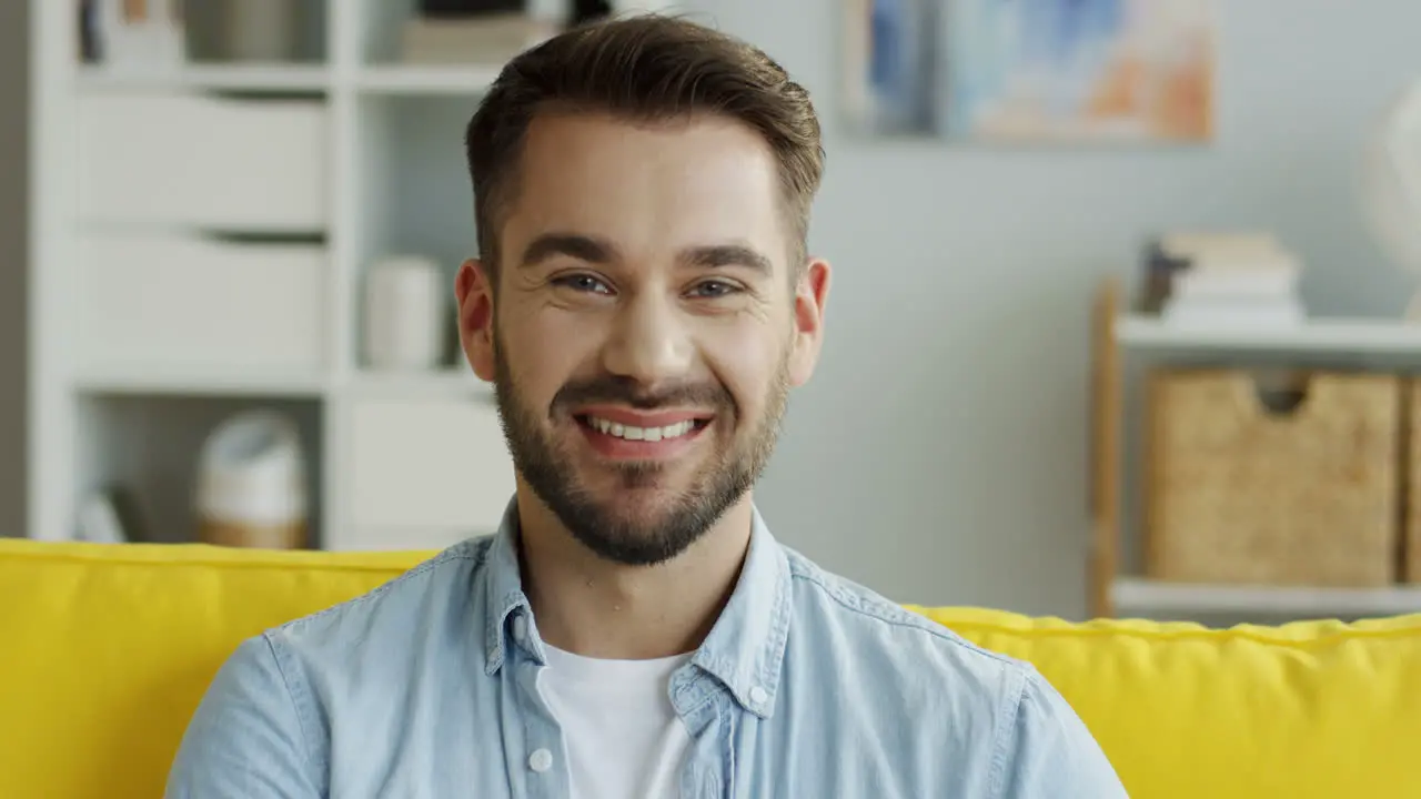 Close Up Of The Attractive Man Looking To The Camera And Smiling In The Living Room