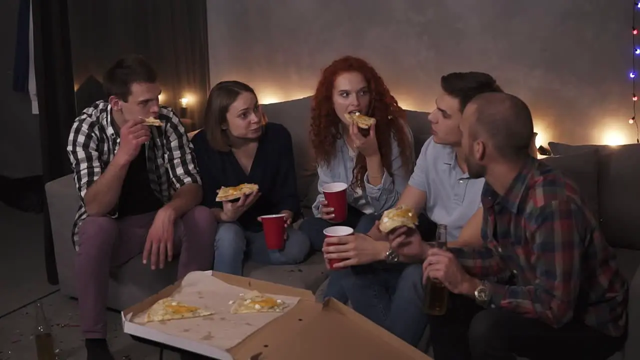 Cheerful Men And Women Are Eating Cheesy Pizza Chatting Relaxing During Indoor Party In Apartment In A Loft Room