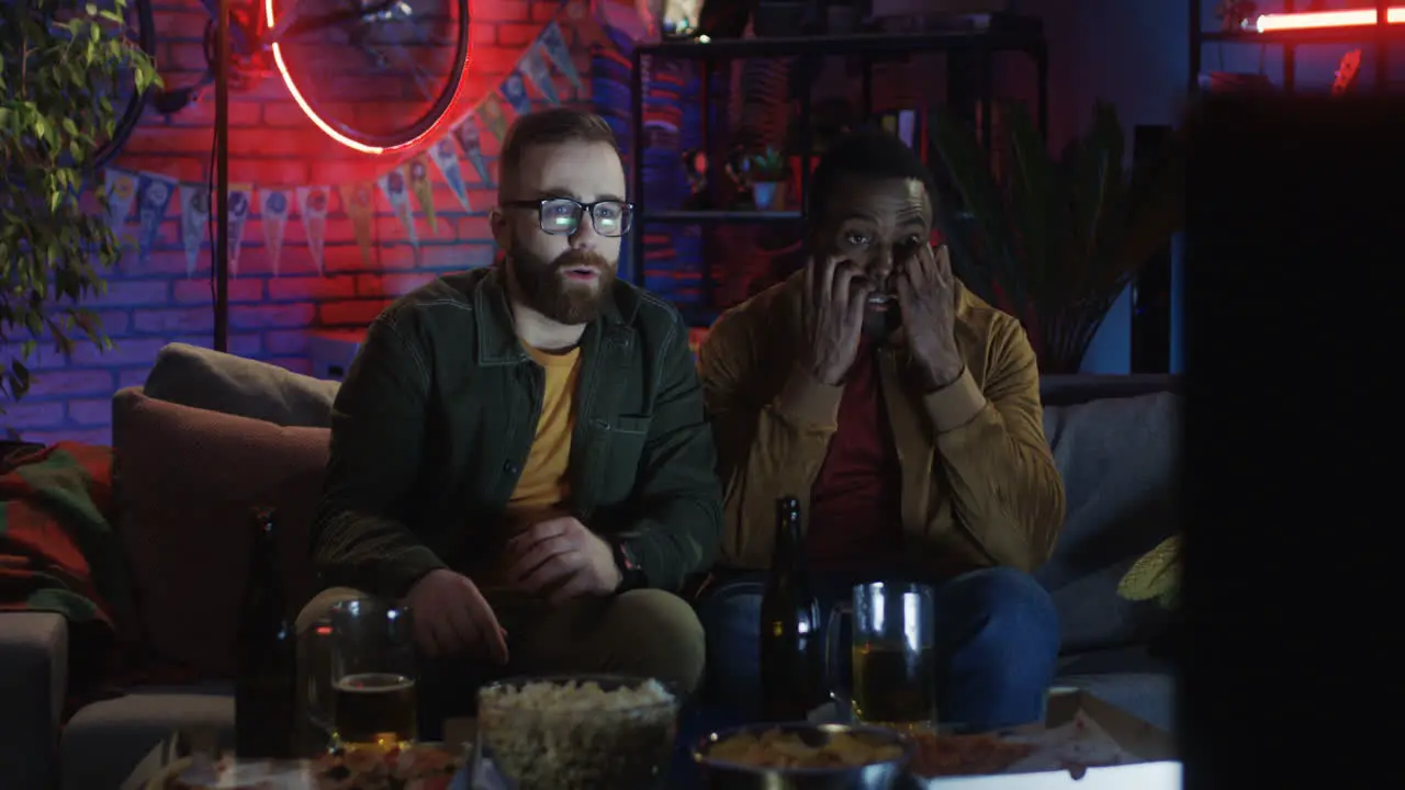 Portrait Shot Of The Two Young Men And American Watching Horror Movie On The Sofa At Home At Night And Being Very Scary