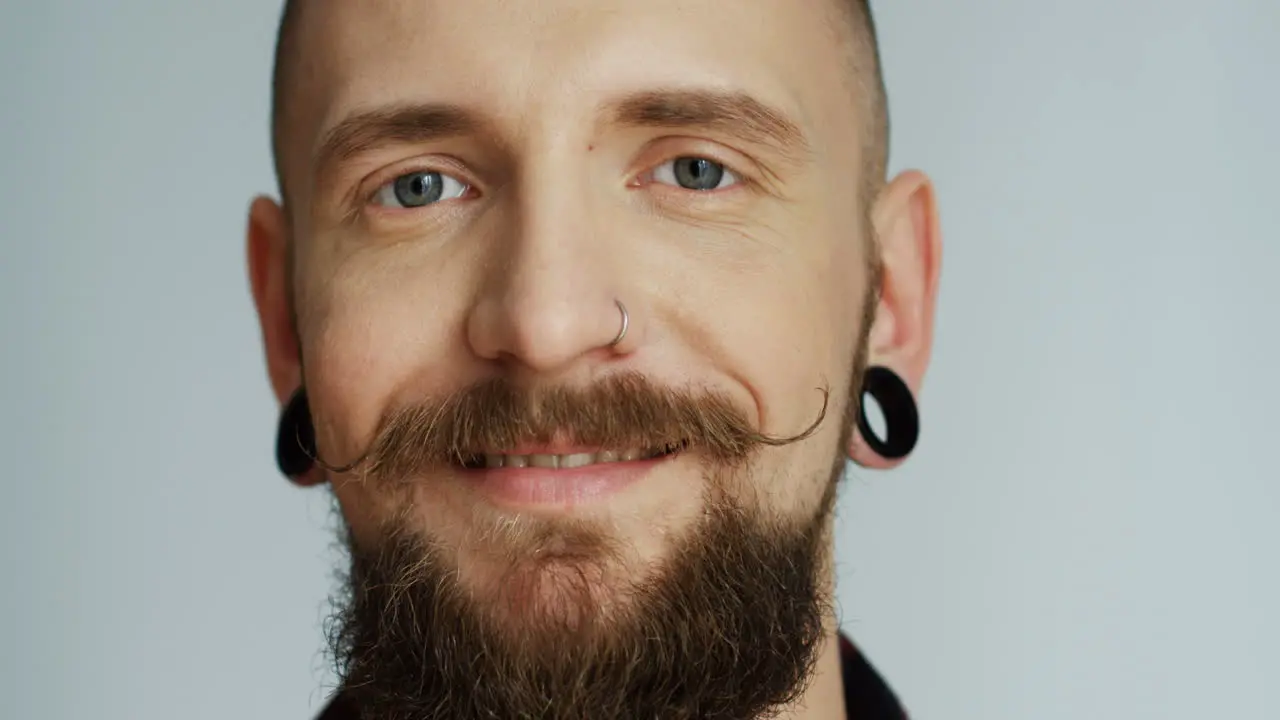 Portrait Of The Smiled Good Looking Hipster Man With Earings Smiling And Looking Straight To The Camera On The White Wall Background