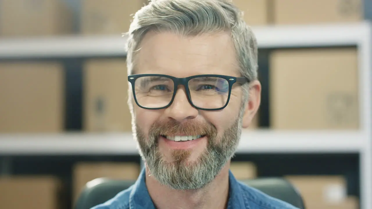 Portrait Of Handsome Male Postman In Glasses Smiling Cheerfully To Camera In Postal Storage Of Parcels