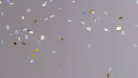 Stationary Shot of White Blue and Gold Confetti Falling Against Grey Background