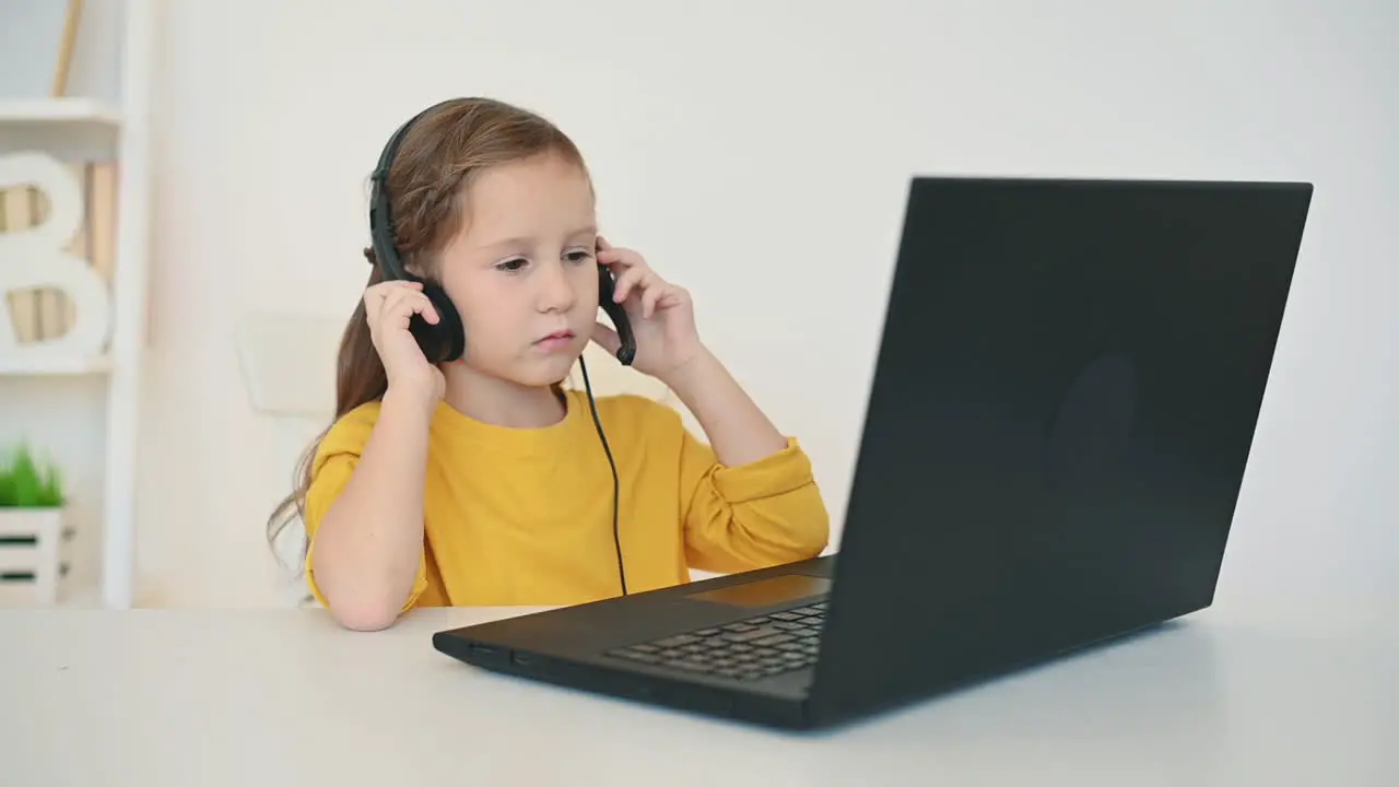 Little Girl With Headphones Uses Laptop At Home