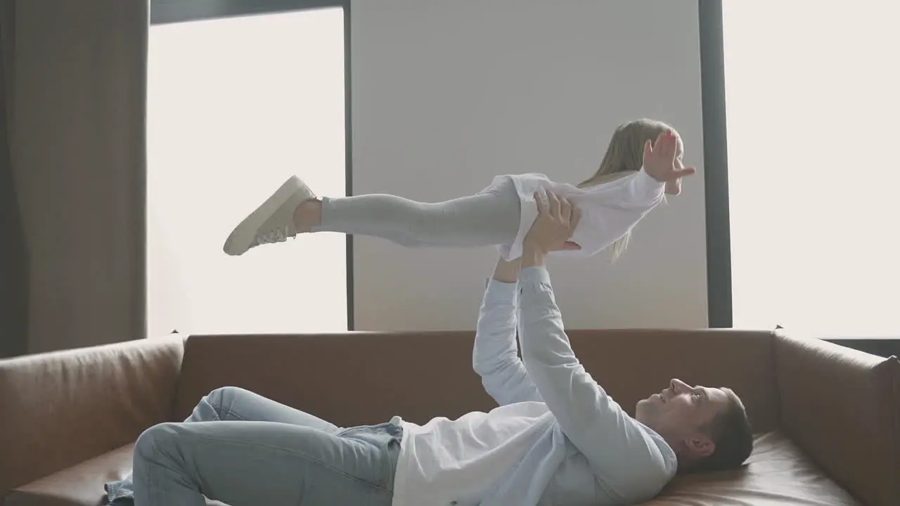 Dad Lifting His Little Daughter Lying On The Sofa At Home