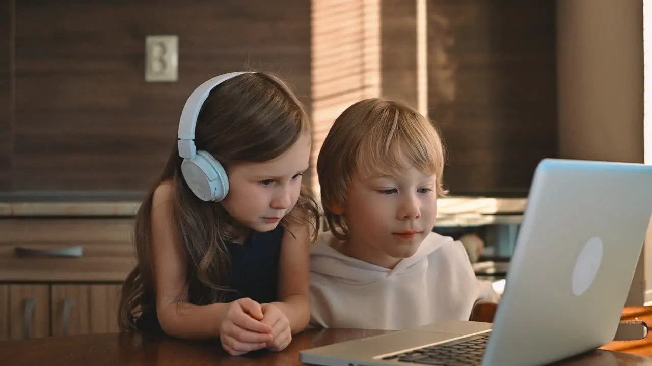 Little Girl And Boy Using A Laptop With Wireless Headphones And Having An Online Class At Home