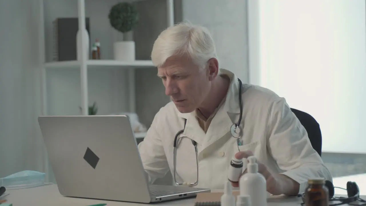 A Grey Haired Middle Aged Doctor Consults On His Laptop The Composition Of A Medicine