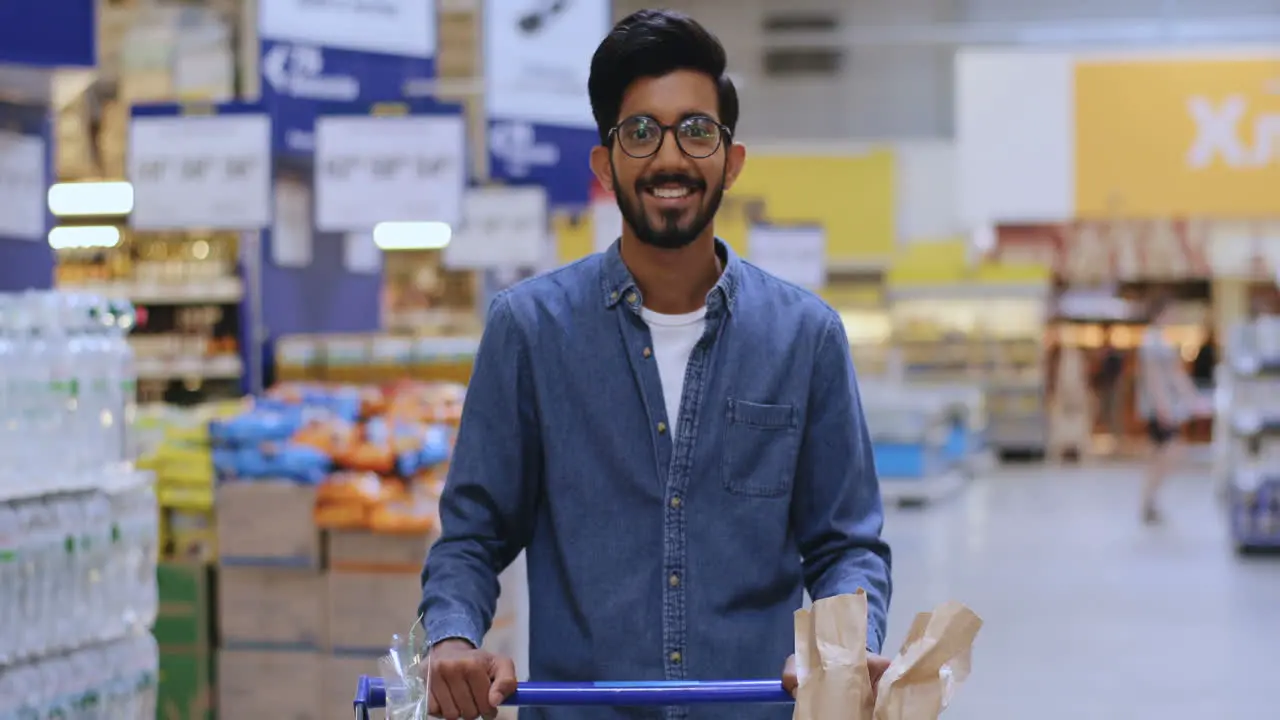 Portrait Of A Tall Boy With Glasses Leaning On The Shopping Cart In The Supermarket Looking Straight At The Camera And Smiling