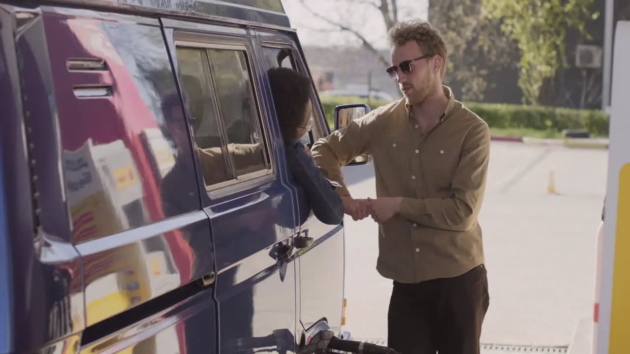 An Young Woman And A Young Man Have A Conversation While Refueling Their Van 1